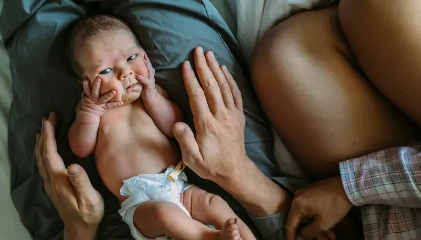 Nyfödd bebis med händer mot ansiktet, tryggt omfamnad av föräldrar. En stund av samsova bebis och närhet.