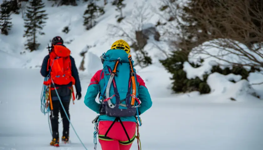 Dwóch alpinistów w zimowych strojach, z plecakami i sprzętem, przemierza ośnieżony teren. To inspiracja, co zabrać w góry zimą.