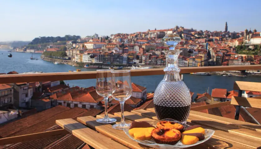 Un bicchiere di late bottled vintage porto, due calici e dolcetti su un tavolo con vista sulla città di Porto.