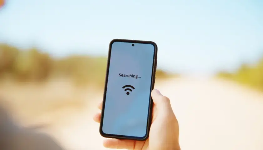 Dłoń trzyma smartfon z napisem "Searching..." i ikoną Wi-Fi na tle drogi.
