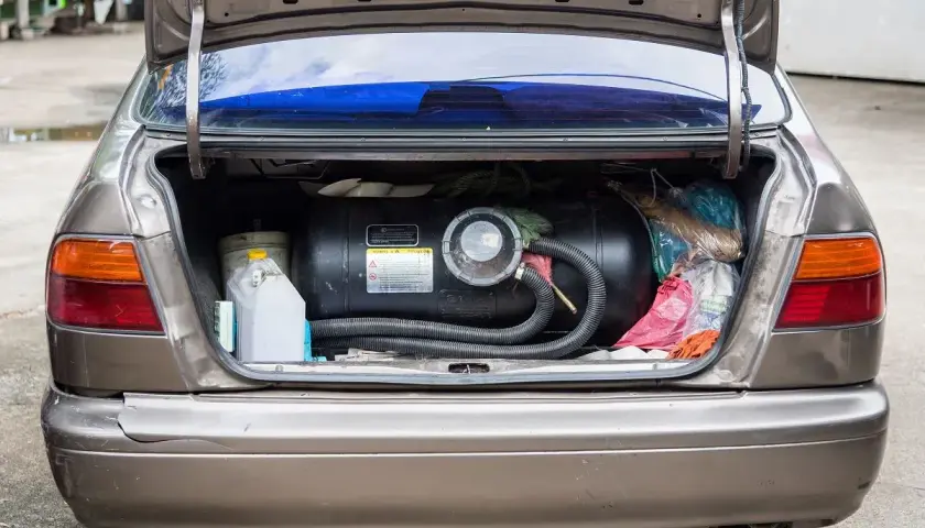 Bagażnik samochodu z zamontowanym zbiornikiem na gaz CNG. Obok kanister i torby z zakupami.