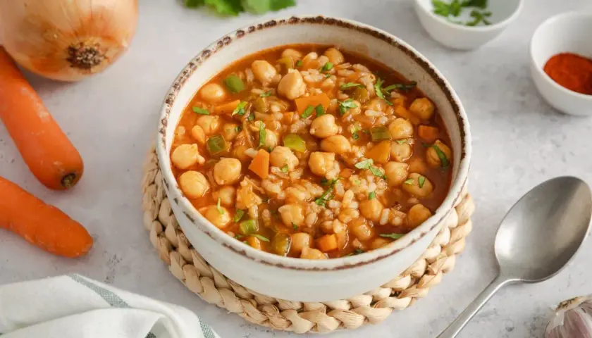 Un reconfortante plato de garbanzos con arroz, zanahorias y pimientos verdes, adornado con perejil fresco.