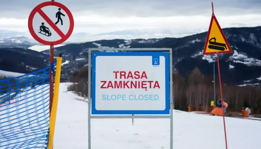 Na stoku narciarskim widoczne są wskaźniki kolejowe: zakaz saneczkarstwa, tablica "Trasa zamknięta" oraz znak ostrzegawczy z ratrakiem.