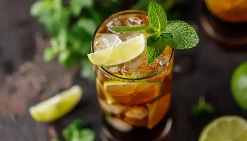 Szklanka z drinkiem Cuba Libre, lodem, plasterkami limonki i listkami mięty.