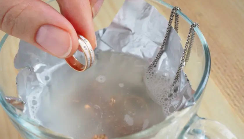 Mano sumerge un anillo en agua con bicarbonato para limpiar metales.