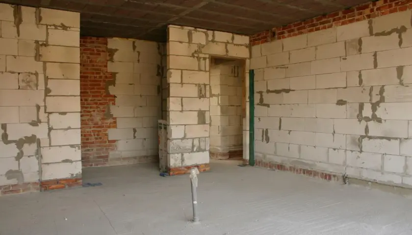 Wnętrze w budowie, ściany z bloczków, widoczne fragmenty cegły, sufit i podłoga przygotowane pod wykończenie. Wkrótce powstanie tu piękny dom z **regips**.