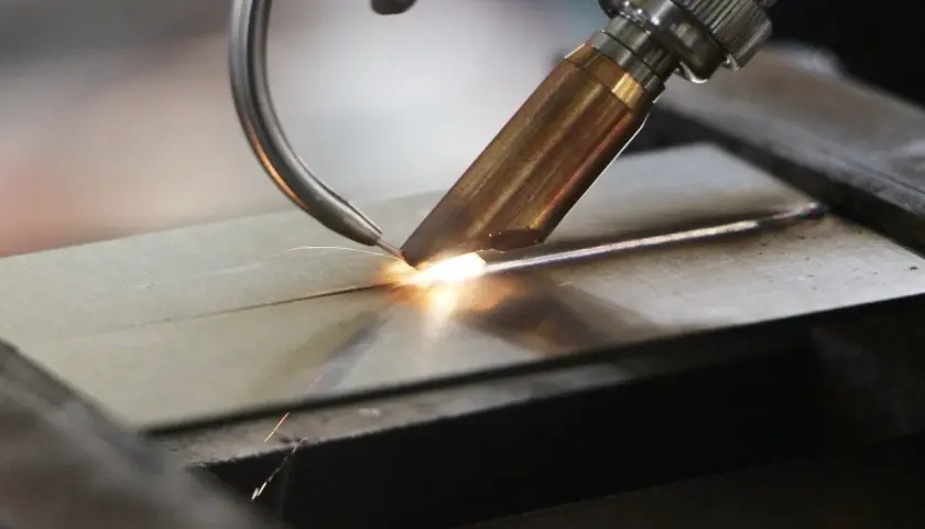 Precyzyjne spawanie laserowe aluminium, tworzące idealne połączenie dwóch elementów. Iskry i jasny łuk świadczą o wysokiej temperaturze procesu.