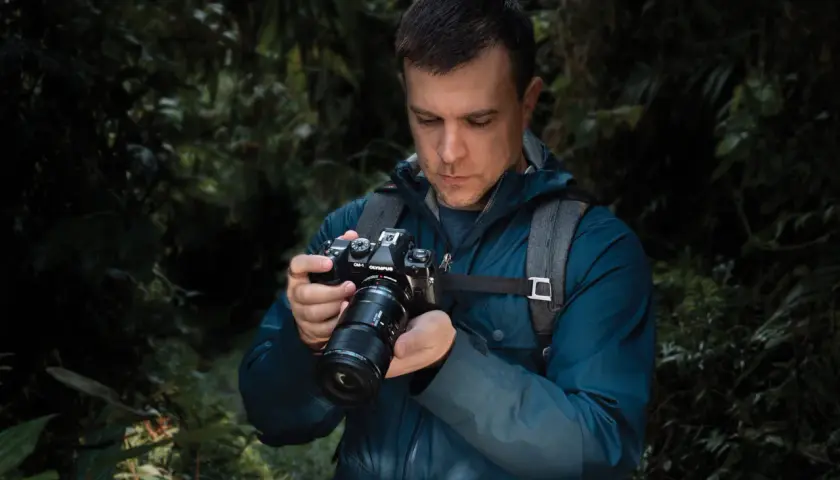Mężczyzna w lesie trzyma aparat OM-1 Olympus, przygotowując się do makrofotografii sprzętu.