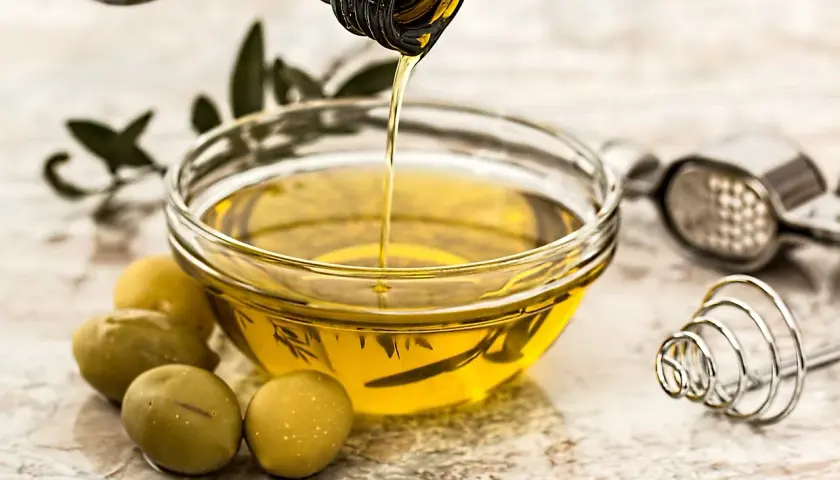 Olio d'oliva versato in una ciotola, pronto per friggere. Olive verdi e un pestello completano la scena.