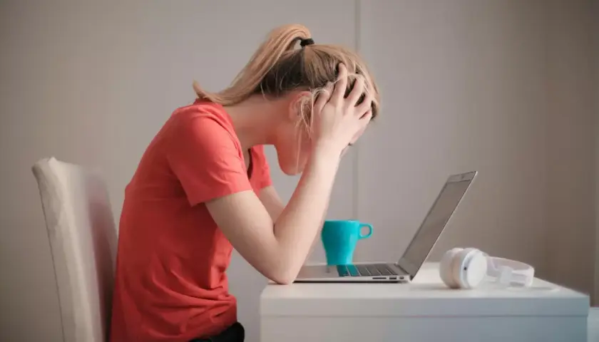 Donna con le mani tra i capelli, frustrata davanti al laptop. La cistite è rabbia repressa, un peso che schiaccia.