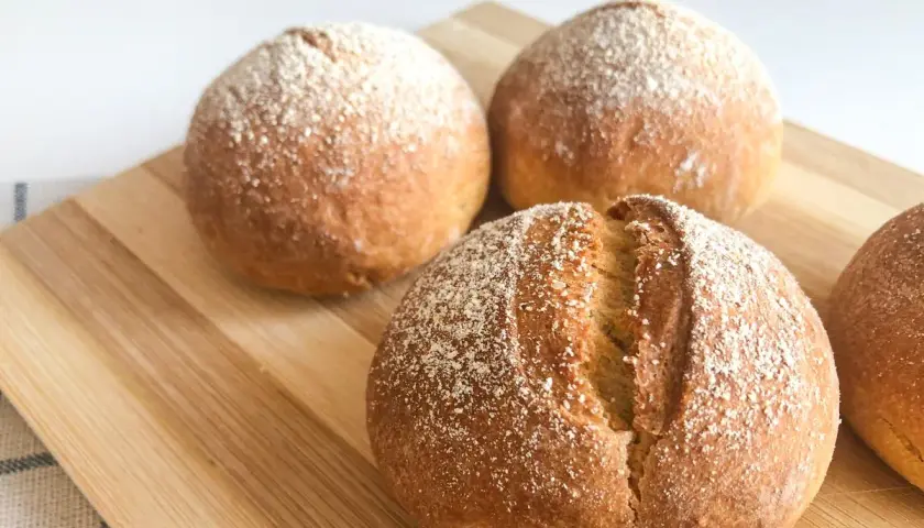 Pane dorato e fragrante, appena sfornato nella friggitrice ad aria, cosparso di farina su un tagliere di legno.
