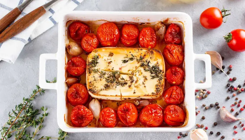 Feta in friggitrice ad aria, circondata da pomodorini arrostiti, aglio e erbe aromatiche. Un piatto semplice e gustoso.