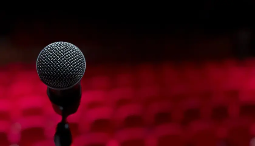 Mikrofon na statywie na tle czerwonych foteli. Chcesz wiedzieć, jak lepiej śpiewać? To miejsce dla Ciebie.
