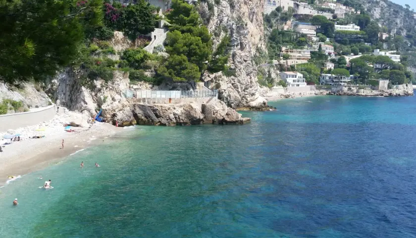 Spiaggia di Eze-sur-Mer con ville aggrappate alla scogliera e acque turchesi cristalline.