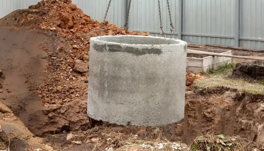 Betonowy krąg opuszczany do wykopu. Zastanawiasz się, ile kosztuje założenie szamba? To pierwszy krok do jego budowy.