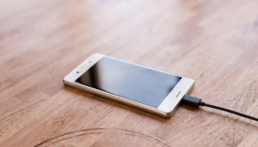 Biały smartfon podłączony do ładowarki. Zastanawiasz się, jaka jest moc ładowarki do telefonu w watach, aby szybko naładować urządzenie.