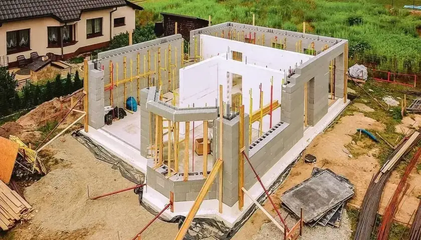 Budowa domu styropianowego w toku. Widać fundamenty, ściany z bloczków i elementy szalunku.
