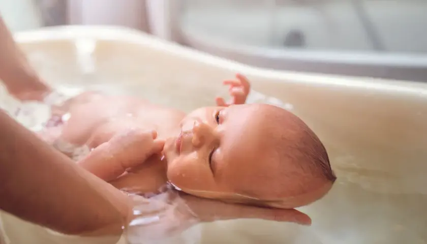 Malutkie dzieci w kąpieli, delikatnie unoszone na wodzie. Rączka rodzica podtrzymuje główkę niemowlaka, tworząc bezpieczną przestrzeń do relaksu.