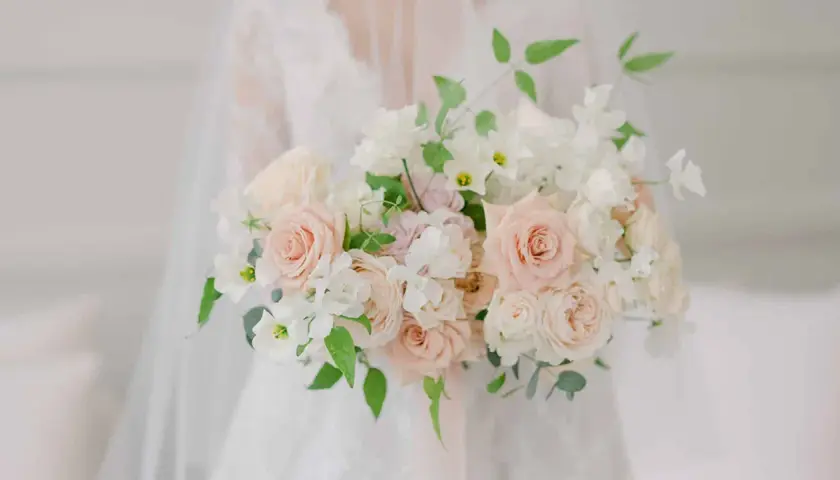 Un bouquet de mariée tombant original, composé de roses douces et de fleurs blanches délicates, drapé sur une robe de mariée.
