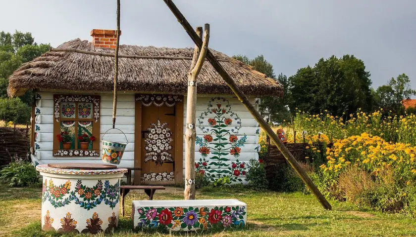 Kolorowy dom z malowanymi kwiatami, studnia i ławka. Zalipie atrakcje zachwycają ludowym pięknem.
