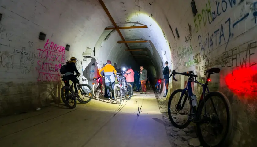 Grupa rowerzystów eksploruje mroczną, graffiti-pokrytą podziemną trasę rowerową, oświetloną latarkami.