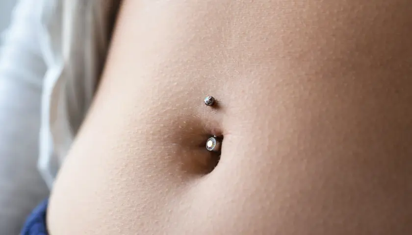 Zbliżenie na brzuch z kolczykiem w pępku. Delikatna skóra, subtelny blask biżuterii. To jest właśnie ten słynny **angie piercing**.