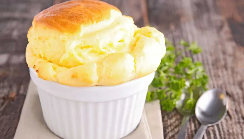 Un délicieux soufflé au fromage, doré et gonflé, servi dans un ramequin blanc sur une table en bois rustique.