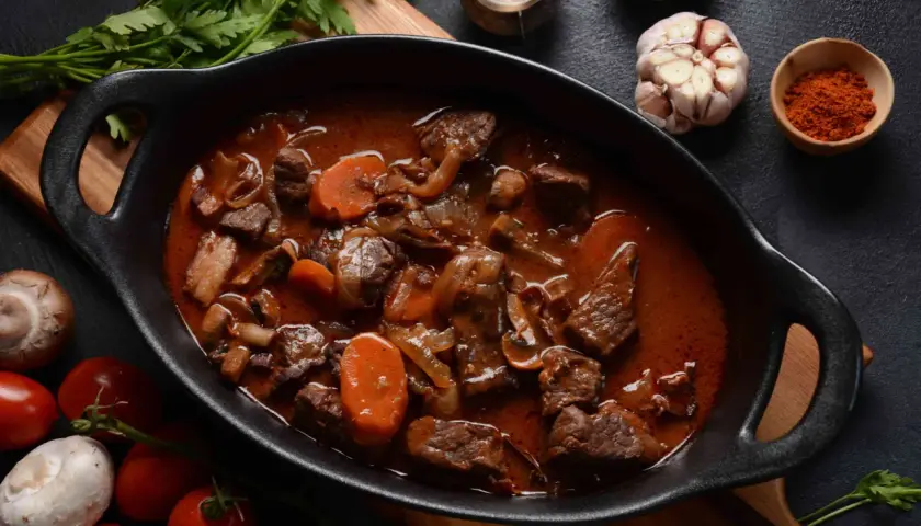 Un riche bœuf bourguignon mijoté, avec des morceaux de viande tendres, des carottes et des champignons, prêt à être dégusté avec un verre de pinot noir.