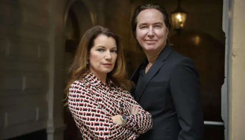 Alexander Ahndoril och en kvinna står nära varandra. Kvinnan bär en mönstrad blus och mannen en mörk kostym.