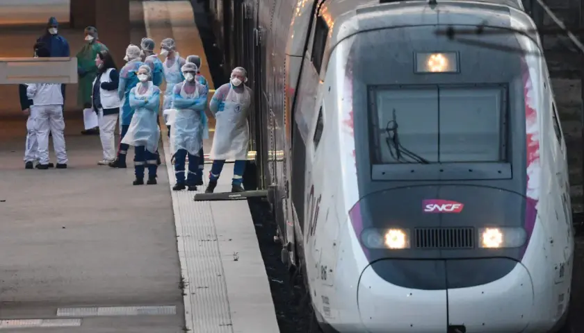 Grupa osób w kombinezonach ochronnych stoi na peronie obok pociągu SNCF.