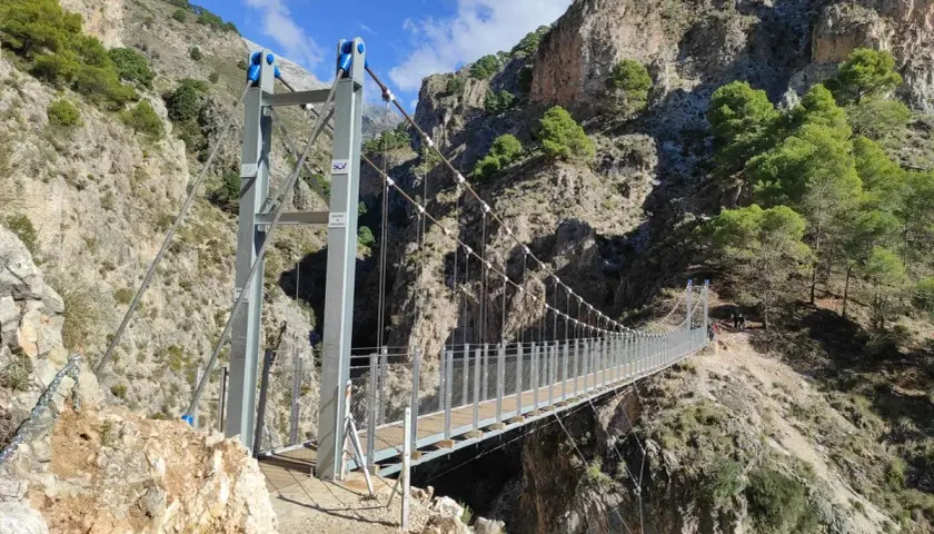 Puente colgante en la ruta del saltillo, con imponentes montañas rocosas y vegetación verde.