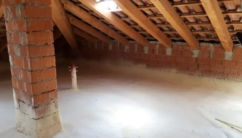Sottotetto in fase di isolamento con schiuma espansa. Si vede la struttura in legno e mattoni, segno che conviene isolare il sottotetto per un maggiore comfort.