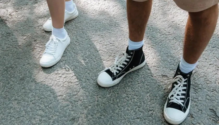 Białe i czarne trampki, idealne buty na długie marsze, stoją na szarej nawierzchni.