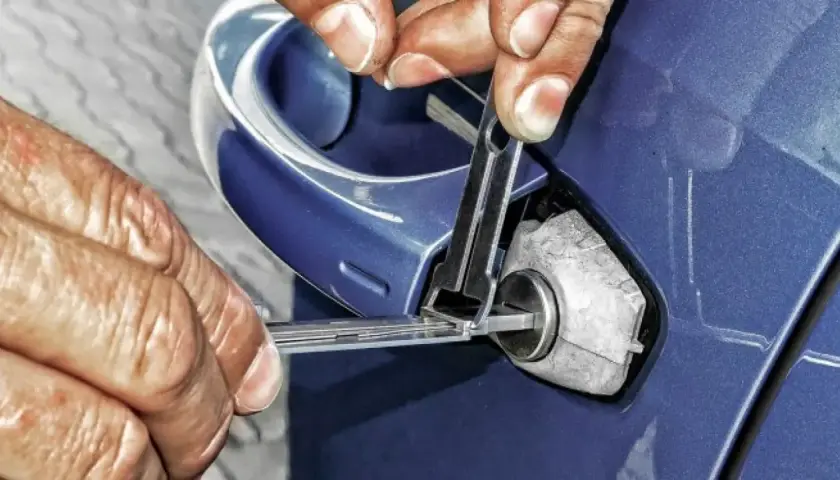 Manos expertas intentan abrir coche sin llave con herramientas especializadas.