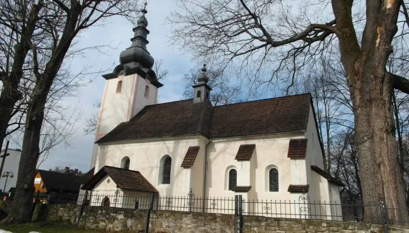 Kościół w Krościenku nad Dunajcem, z charakterystyczną wieżą i dachem, otoczony drzewami.