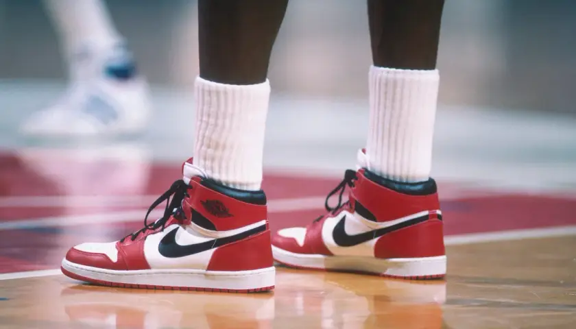 Rote und weiße Air Jordan 1 Sneaker mit schwarzem Nike-Logo auf einem Basketballplatz. Ein ikonisches Stück der Geschichte des Nike-Unternehmens.