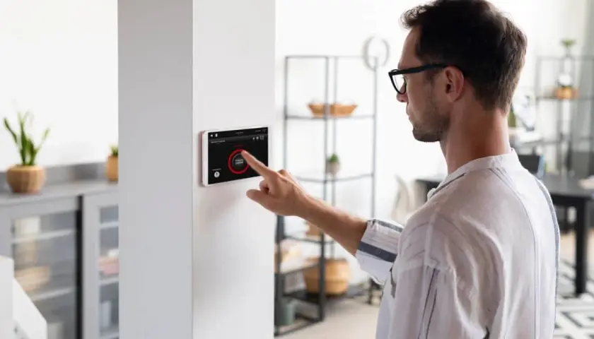 Hombre interactúa con pantalla táctil de domótica, controlando luces y seguridad. Los sensores domotica hacen el hogar inteligente.