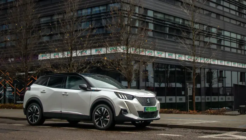 Biały Peugeot e-2008 zaparkowany przed nowoczesnym budynkiem.