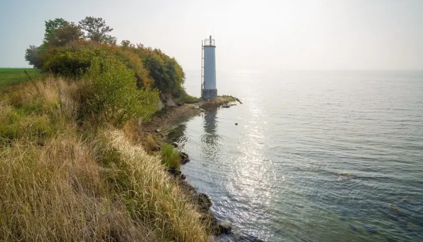 Leuchtturm auf der Halbinsel Zudar, umgeben von üppiger Vegetation und dem glitzernden Meer.