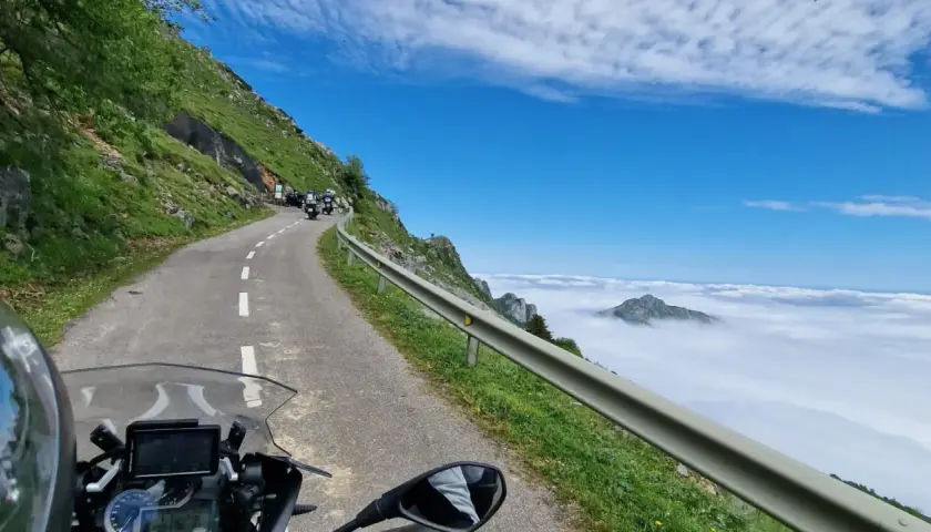 Motociclistas en un viaje por carretera, con un paisaje montañoso y nubes. El significado de este trip km es la aventura.