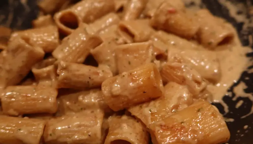 En närbild på rigatoni pasta i en krämig ost och skinksås. Pastan är täckt av såsen som ser smakrik ut.