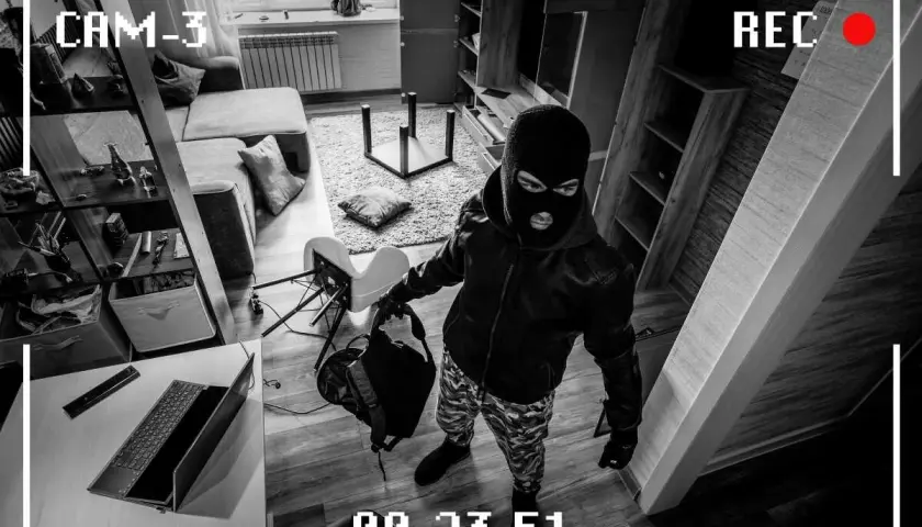 Złodziej w masce na twarzy, z torbą w ręku, przygotowuje się do kradzieży. W tle widać przewrócone meble i bałagan, jakby po szybkim przeszukaniu. To nie jest zwykły dzień, to moment, gdy oczep zostaje zdjęty z głowy, a złoczyńca działa.