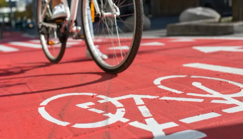 Rowerzysta nabiera prędkości na czerwonej ścieżce rowerowej, gdzie białe symbole rowerów wyznaczają trasę.