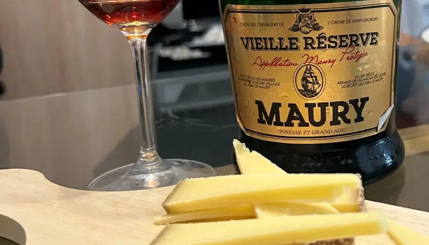 Verre de vin et fromage sur planche en bois, à côté d'une bouteille de Maury. La question est : que boire avec du fromage ?