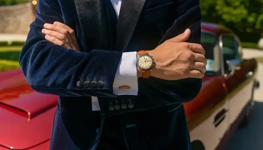 Elegancki mężczyzna w granatowym aksamitnym garniturze i białej koszuli pokazuje, jak nosić zegarek do koszuli. Klasyczny styl.