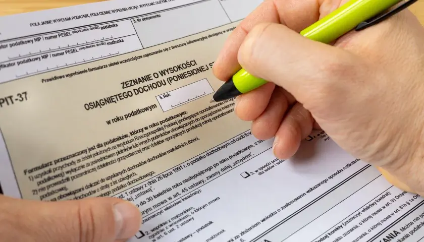 Dłoń z zielonym długopisem wypełnia formularz PIT-37.