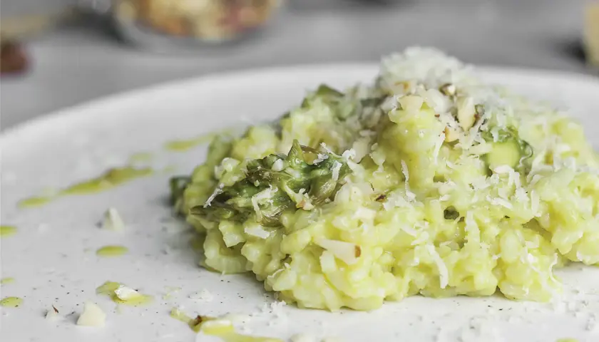 Kremowe risotto ze szparagami, posypane parmezanem i migdałami, na białym talerzu.