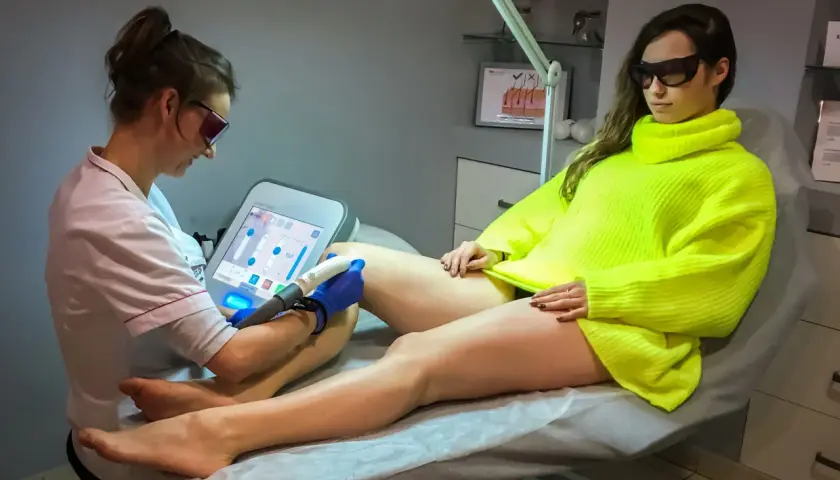 Specjalistka wykonuje depilację laserową nogi klientki. Czy depilacja laserowa boli? Zależy od indywidualnego progu bólu.