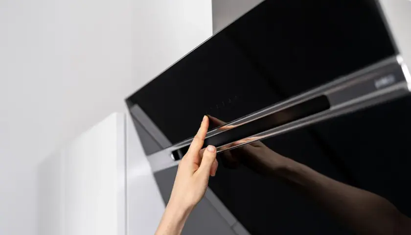 Mano tocando controles táctiles de campana extractora decorativa. Guía para como instalar una campana extractora decorativa.
