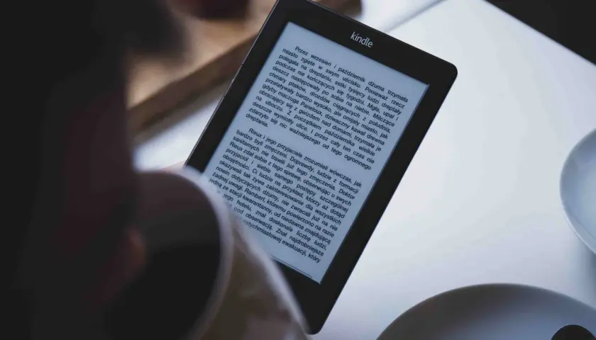 Osoba czyta książkę na czytniku Kindle. Tekst na ekranie jest w formacie epub, a historia opowiada o dżumie w mieście.